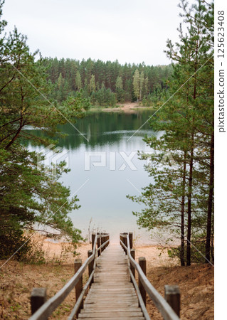 Wooden pier on the background of a beautiful lake summer dawn landscape. View from the shore Wooden pier on the background of a beautiful lake summer dawn landscape. View from the shore 125623408