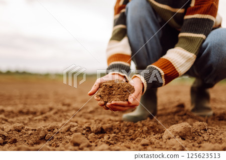 Young female farmer's hands touch dry soil in an agricultural field. Gardening and ecology concept. 125623513