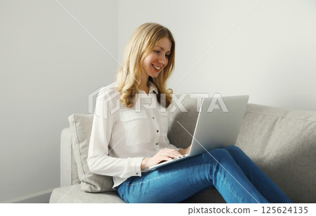 Happy modern woman working with laptop, freelancer girl sitting on a couch in the living room 125624135