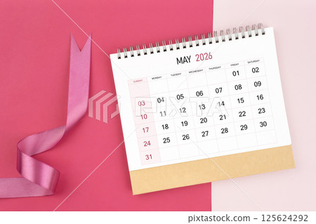 May 2026 desk calendar and pink ribbon on pink background. 125624292