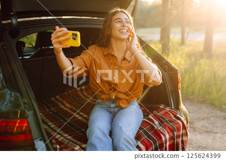 Happy Woman is resting in trunk of car and taking selfie. Selfie time. Lifestyle, travel Happy Woman is resting in trunk of car and taking selfie. Selfie time. Lifestyle, travel 125624399