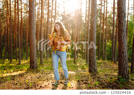 Young woman using mobile application to navigate in autumn forest. Happy tourist trying to find way 125624416