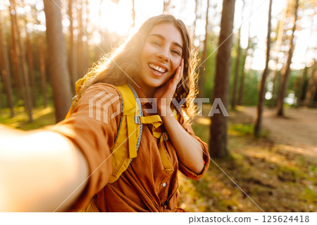Beautiful woman taking picture of herself while walking in sunny forest. Selfie in nature. Adventure Beautiful woman taking picture of herself while walking in sunny forest. Selfie in nature. Adventure 125624418
