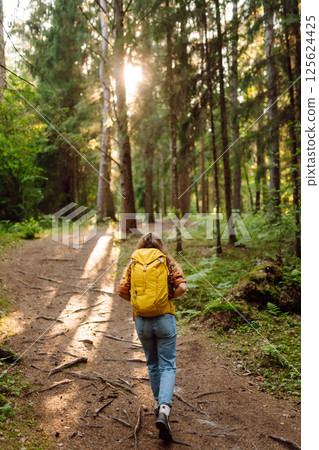 Tourist woman hiking alone in thick autumn forest. Stylish female looks for pathway among trees. Tourist woman hiking alone in thick autumn forest. Stylish female looks for pathway among trees. 125624425