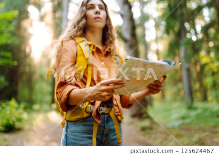A traveler woman stands in a lush forest, examining a map with a focused expression 125624467