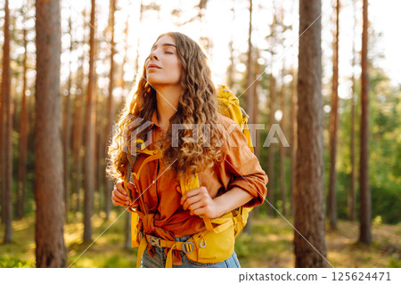 Tourist woman hiking alone in thick autumn forest. Stylish female looks for pathway among trees. 125624471