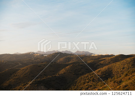 Softly lit hills and distant mountains under a golden sunset, creating a peaceful natural landscape 125624711
