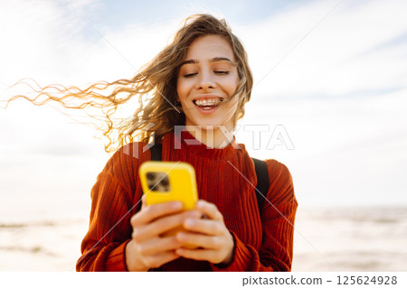 Young woman using mobile phone at beach. Cold weather. Autumn. Blogging, communication 125624928
