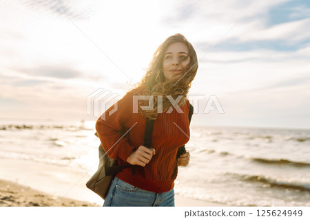 As she walked along the beach, the woman tourist adjusted her backpack, taking in the salty sea air 125624949