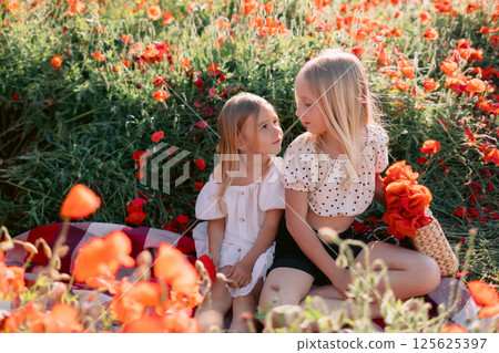 Sisters girls sitting on a plaid in blooming poppy field, sunny summer day 125625397