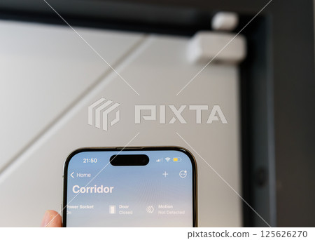 A close-up of a smartphone displaying a smart home interface, showing real-time security status with Door Sensor in Background A close-up of a smartphone displaying a smart home interface, showing real-time security status with Door Sensor in Background 125626270