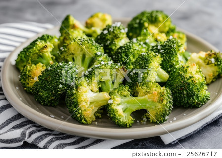 Close-up of roasted broccoli florets sprinkled with sea salt on a ceramic plate. Healthy vegan meal served on a striped napkin, ideal for clean eating and plant-based food concepts. Copy space Close-up of roasted broccoli florets sprinkled with sea salt on a ceramic plate. Healthy vegan meal served on a striped napkin, ideal for clean eating and plant-based food concepts. Copy space 125626717