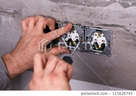 A worker installs an electrical outlet into a wall using a screwdriver A worker installs an electrical outlet into a wall using a screwdriver 125626745