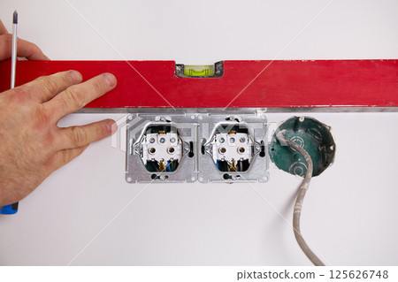 The worker installs an electrical socket in the wall 125626748