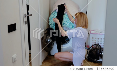 Woman checks freshly washed black pants in the utility room, showcasing the everyday tasks of domestic life in a well kept home Woman checks freshly washed black pants in the utility room, showcasing the everyday tasks of domestic life in a well kept home 125626890