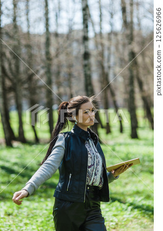A beautiful girl in leather pants and a bomber jacket with a tablet in a spring park.  125626966