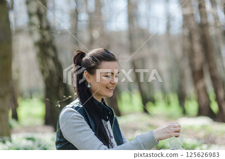 A girl in the park opens a bottle of water. A woman is resting in the forest and sitting with a bottle of water in her hands.  125626983
