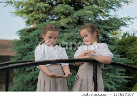 Girls in white blouses look innocent and gentle. The railing with the snail unites their gaze and emotion.  125627107