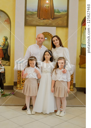 A festive family has gathered in the church at the moment of an important event for the eldest child. Two twin girls and their sister in elegant attire stand beside their mother and father. A festive family has gathered in the church at the moment of an important event for the eldest child. Two twin girls and their sister in elegant attire stand beside their mother and father. 125627468