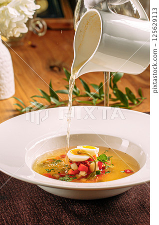 Pouring bouillon in a plate with soup filling 125629113
