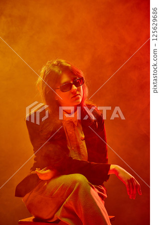 Woman in blazer and sunglasses stares into distance 125629686