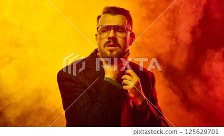 Man in glasses clutches throat and tie with dramatic facial tension inside red-orange fog as if gasping for relief 125629701