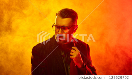 Man in pinstripe suit adjusts tie with firm expression amid thick orange fog symbolizing control under pressure Man in pinstripe suit adjusts tie with firm expression amid thick orange fog symbolizing control under pressure 125629702