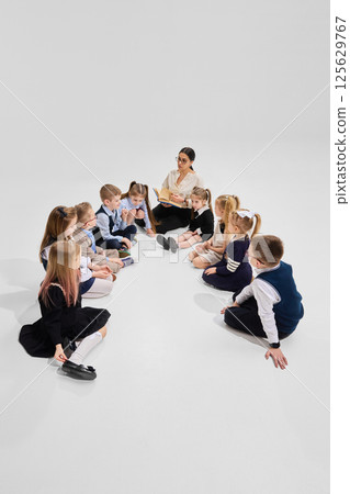 Smiling students listening to storytime as teacher reads aloud from book in classroom circle. Concept of joy of reading Smiling students listening to storytime as teacher reads aloud from book in classroom circle. Concept of joy of reading 125629767