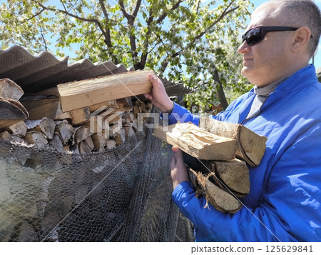 Close-up of a woodpile in the yard. A man takes firewood to light the stove with firewood. Heating the house with firewood in the oven. 125629841