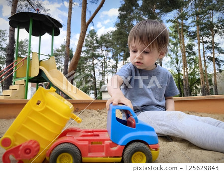 Happy childhood, a child playing in a sandbox with a toy car on an outdoor playground. little boy playing with toy car Happy childhood, a child playing in a sandbox with a toy car on an outdoor playground. little boy playing with toy car 125629843