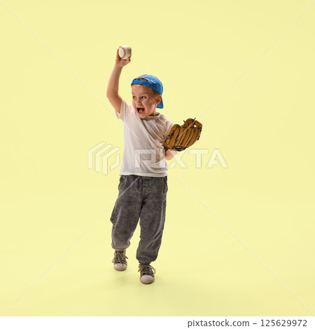 Happy boy holding baseball and glove smiling and shouting of joy against yellow background. Happy boy holding baseball and glove smiling and shouting of joy against yellow background. 125629972