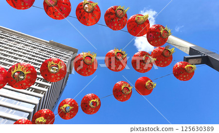 Garland of bright red Chinese lanterns against sky and modern city building, celebrating festive traditions in oriental style. 125630389