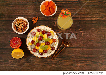 Kitchen background with fruit salads with soft grain cottage cheese, yogurt, dragon fruit, kiwi, mango, oranges, nuts, orange juice and grapes. Healthy light breakfast with ingredients, 125630794