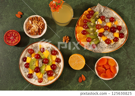 Kitchen background with fruit salads with soft grain cottage cheese, yogurt, dragon fruit, kiwi, mango, oranges, nuts, orange juice and grapes. Healthy light breakfast with ingredients, Kitchen background with fruit salads with soft grain cottage cheese, yogurt, dragon fruit, kiwi, mango, oranges, nuts, orange juice and grapes. Healthy light breakfast with ingredients, 125630825