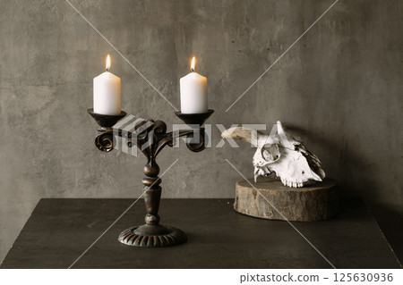 Beautiful vintage brass candelabrum with two burning candles and goats skull in the dark, atmospheric image. Beautiful vintage brass candelabrum with two burning candles and goats skull in the dark, atmospheric image. 125630936