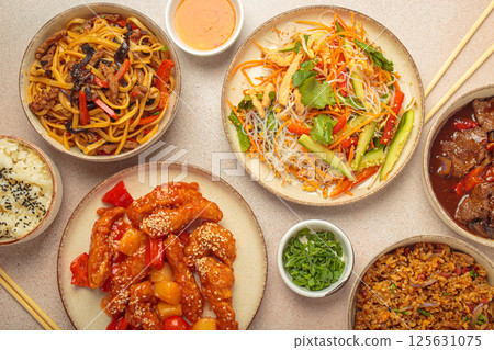 Variety of Chinese food dishes top view on table with chopsticks, light beige background, cuisine of China 125631075