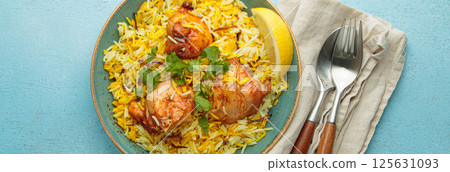 Traditional Indian dish chicken biryani with cilantro and lemon in a bowl top view on blue background Traditional Indian dish chicken biryani with cilantro and lemon in a bowl top view on blue background 125631093