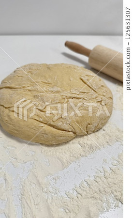 Freshly prepared dough on a floured surface with a rolling pin nearby for baking activities concept Freshly prepared dough on a floured surface with a rolling pin nearby for baking activities concept 125631307