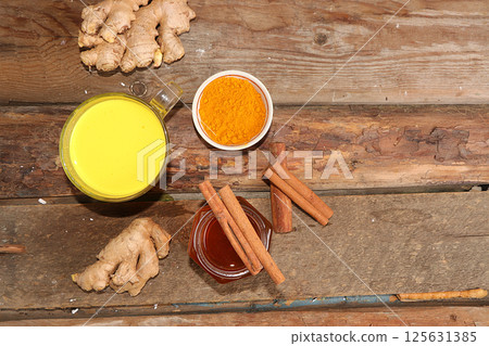 Healthy drink of golden turmeric latte with ginger root, cinnamon sticks, turmeric powder and honey, spices for Ayurvedic medicine. Alternative medicine concept, has a strong anti-inflammatory effect, 125631385