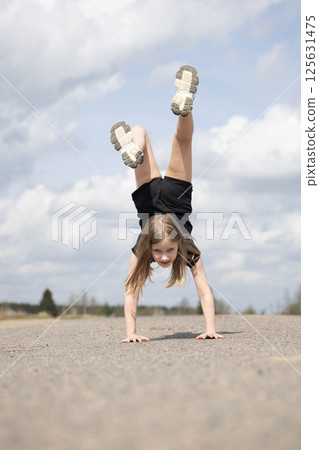 Little girl stands on her hands upside down Little girl stands on her hands upside down 125631475