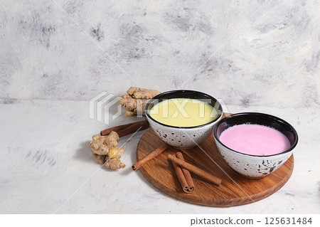 Turmeric latte and pink golden milk for a better sleep, ginger and cinnamon on a gray table, a fashionable relaxing drink, has antioxidant properties, helps detoxify the body, a place for text Turmeric latte and pink golden milk for a better sleep, ginger and cinnamon on a gray table, a fashionable relaxing drink, has antioxidant properties, helps detoxify the body, a place for text 125631484