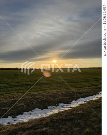 Sunset over a green field with melting snow in early spring 125631494