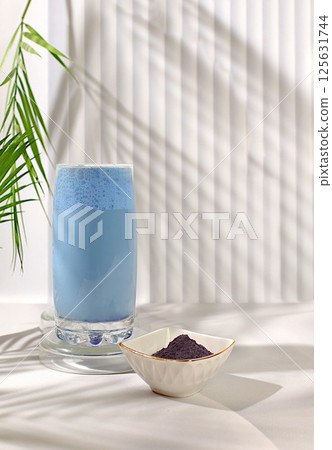 Blue tea matcha latte with milk on elegant kitchen sunny background with palm leaves and matcha powder. Traditional Indian drink rich in antioxidants used for weight loss and treatment 125631744