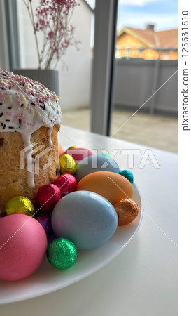Colorful Easter cake surrounded by vibrant decorative eggs on a white plate  125631810