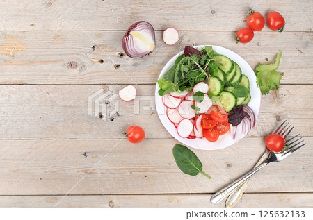Green vegetable salad with cherry tomatoes, cucumber, radish and fresh arugula, detox diet. Healthy natural breakfast for weight loss, cholesterol and GMO free, selective focus, rustic style, place 125632133