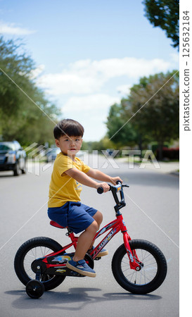 Young Child Riding a Small Bicycle on a Sunny Suburban Street During Daytime 125632184