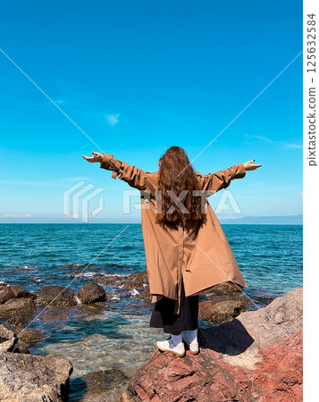 Young caucasian female enjoying ocean view with open arms on rocky coastline Young caucasian female enjoying ocean view with open arms on rocky coastline 125632584