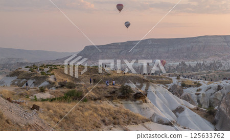 People watching a beautiful sunrise with colorful hot air balloons flying in clear morning sky aerial timelapse in Cappadocia, Turkey 125633762