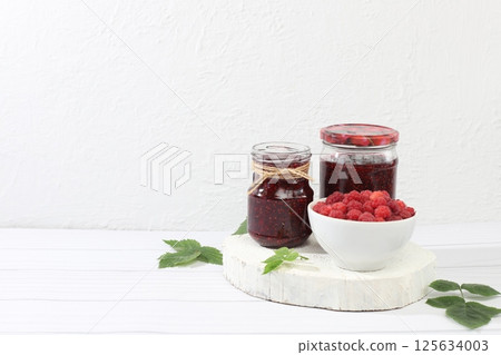 Village harvest, jars of raspberry jam on light wooden background with leaves, shop banner and advertisement, healthy natural food concept, breakfast 125634003