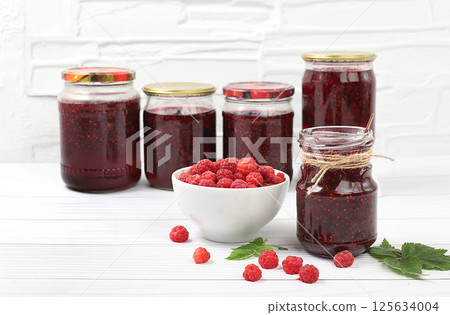 Jars of raspberry jam on a light wooden background with leaves, banner and shop advertisement, healthy natural food concept, home canning concept, Village harvest, breakfast with ingredients, 125634004